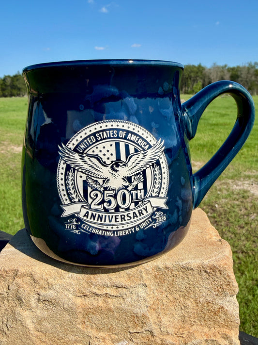 Navy blue mug with 250th Anniversary design on a stone surface with grass and trees in the background