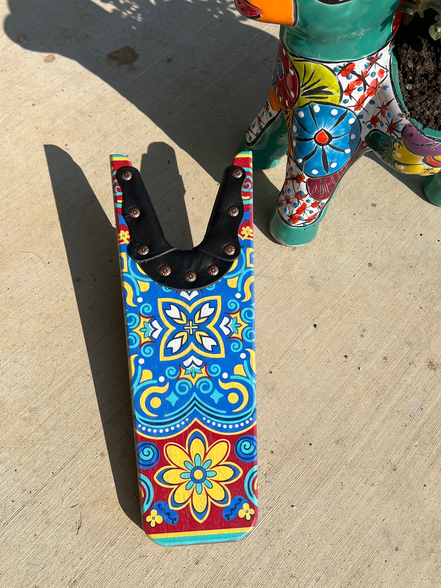 Colorful patterned tool belt on a concrete surface with a colorful ceramic object in the background.