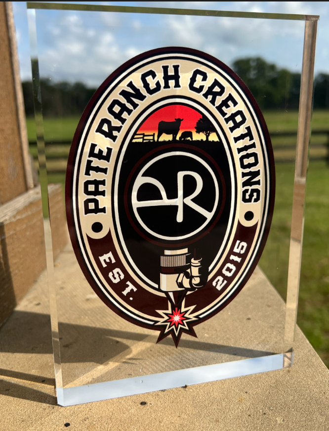 Clear acrylic plaque with 'Rodeo Ranch Creations' logo on a wooden surface with a blurred outdoor background.
