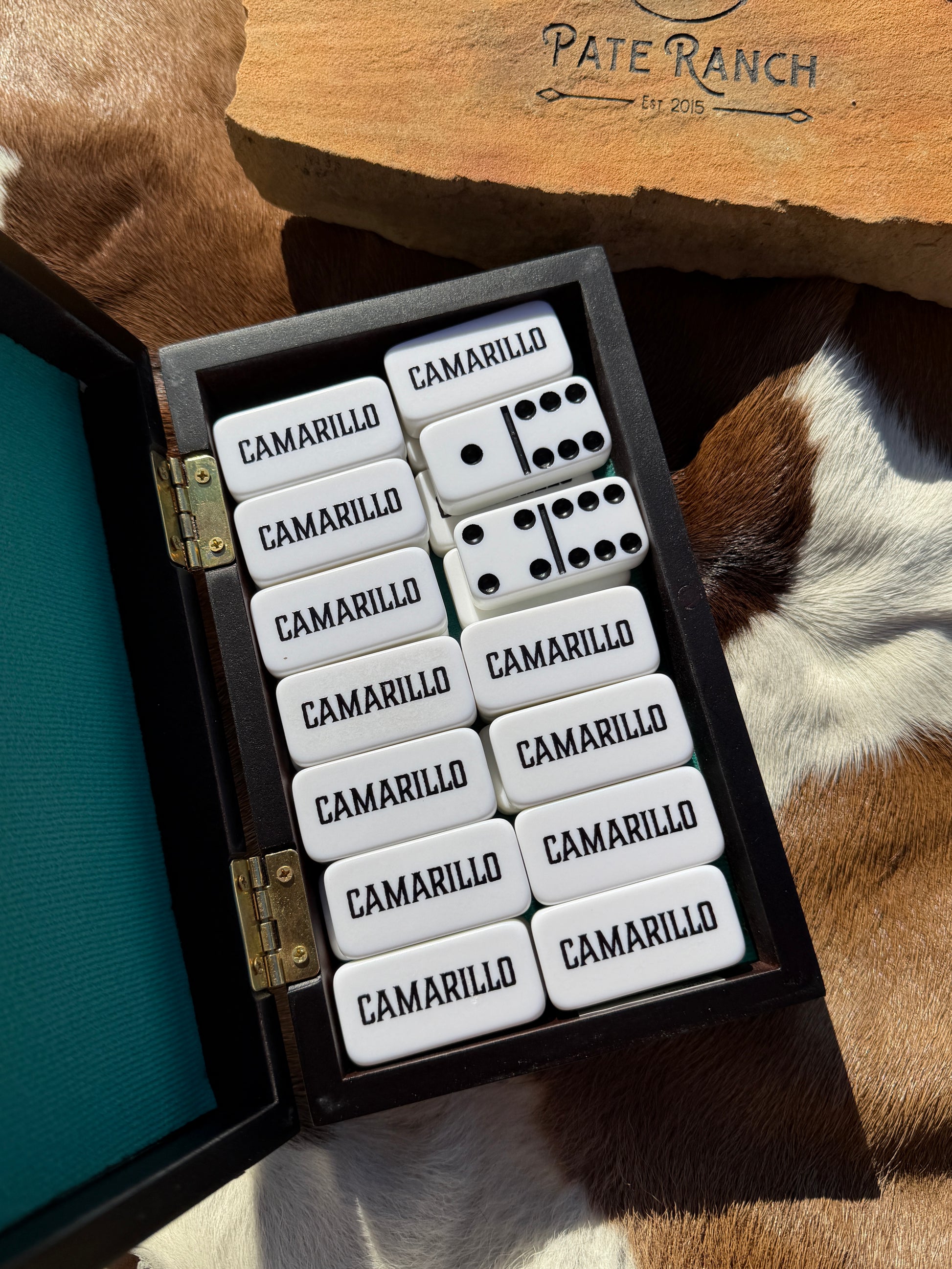 Set of dominoes in a wooden box on a textured surface with 'Pate Ranch' branding.