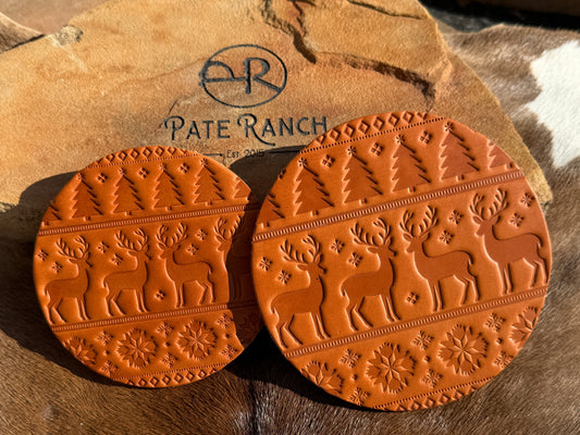 Two brown leather coasters with deer patterns on a stone surface, featuring the 'Pate Ranch' logo.