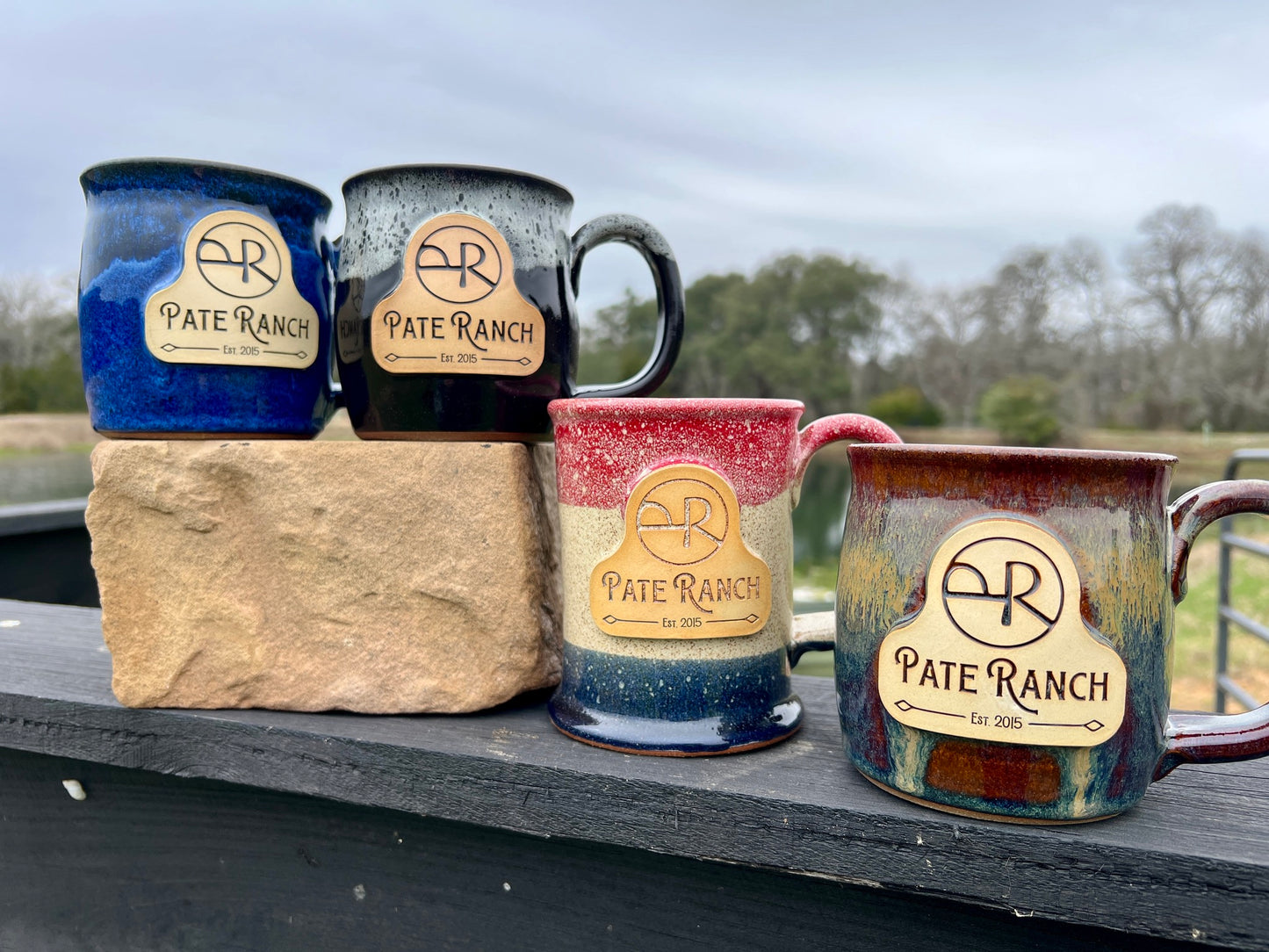 Four ceramic mugs with 'Pate Ranch' branding on a stone block outdoors.