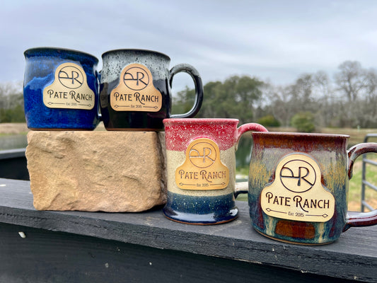 Four ceramic mugs with 'Pate Ranch' branding on a stone block outdoors.