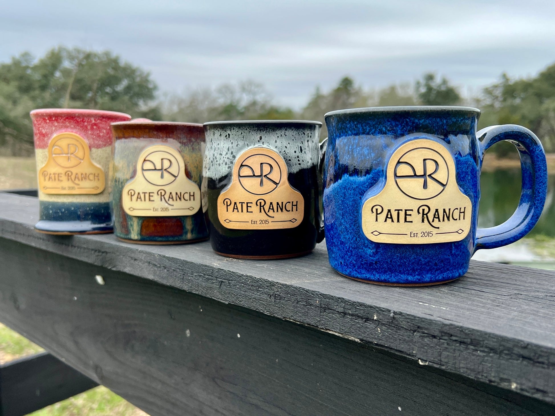 Four ceramic mugs with 'Pate Ranch' branding on a wooden surface outdoors.