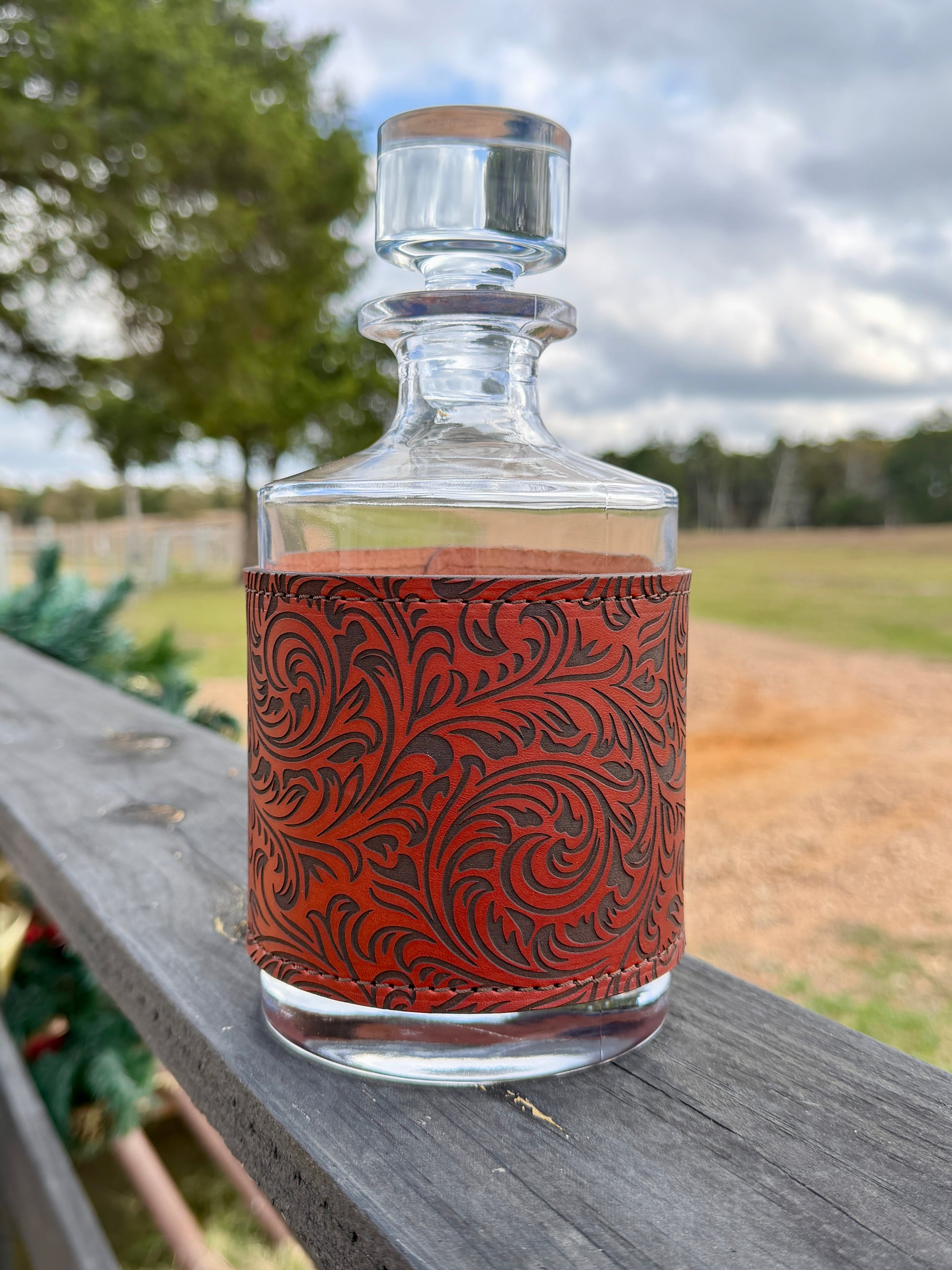 Glass decanter with leather wrap on a wooden surface outdoors