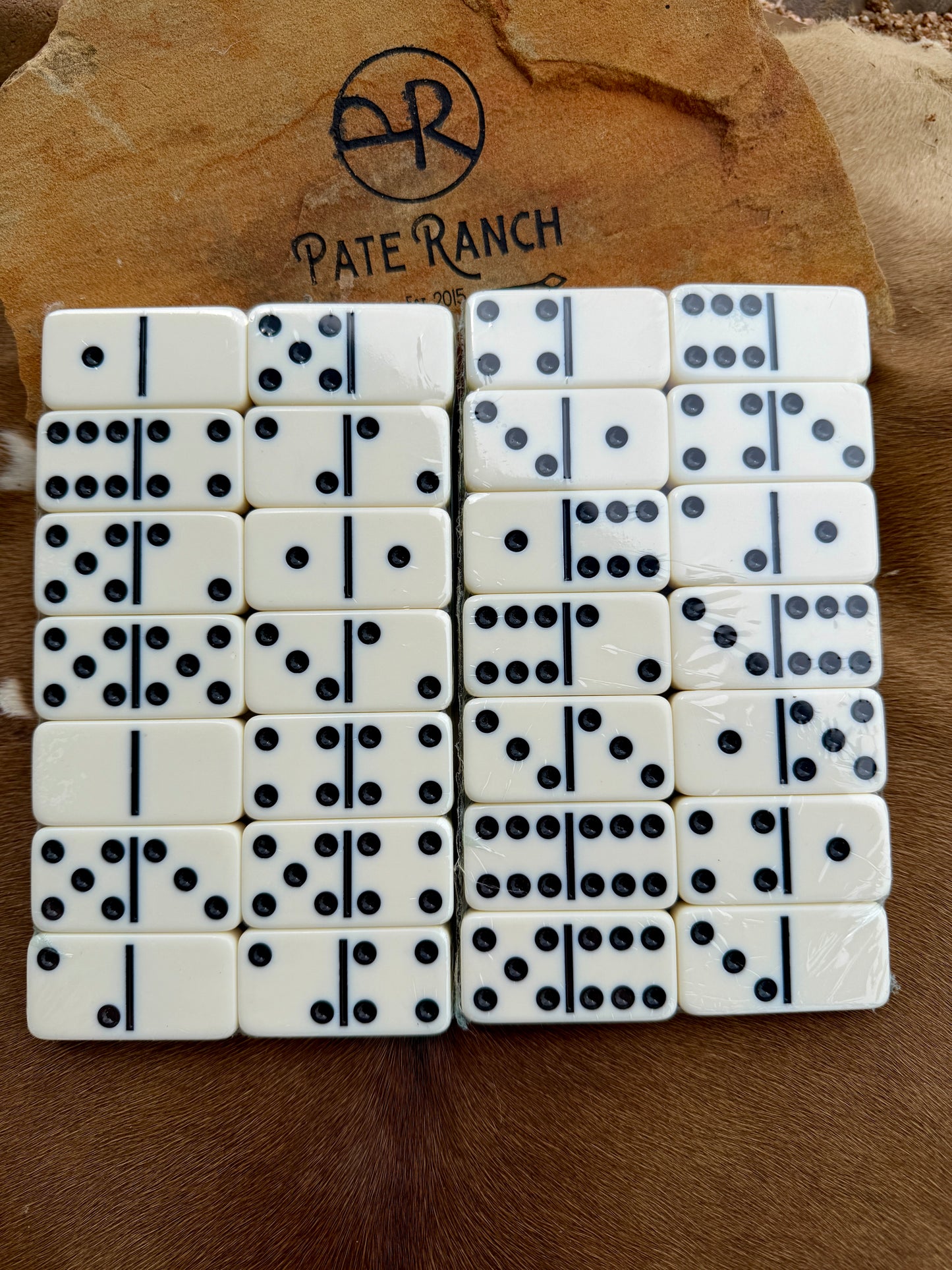 Set of dominoes with black dots on a wooden surface with 'Pate Ranch' branding.