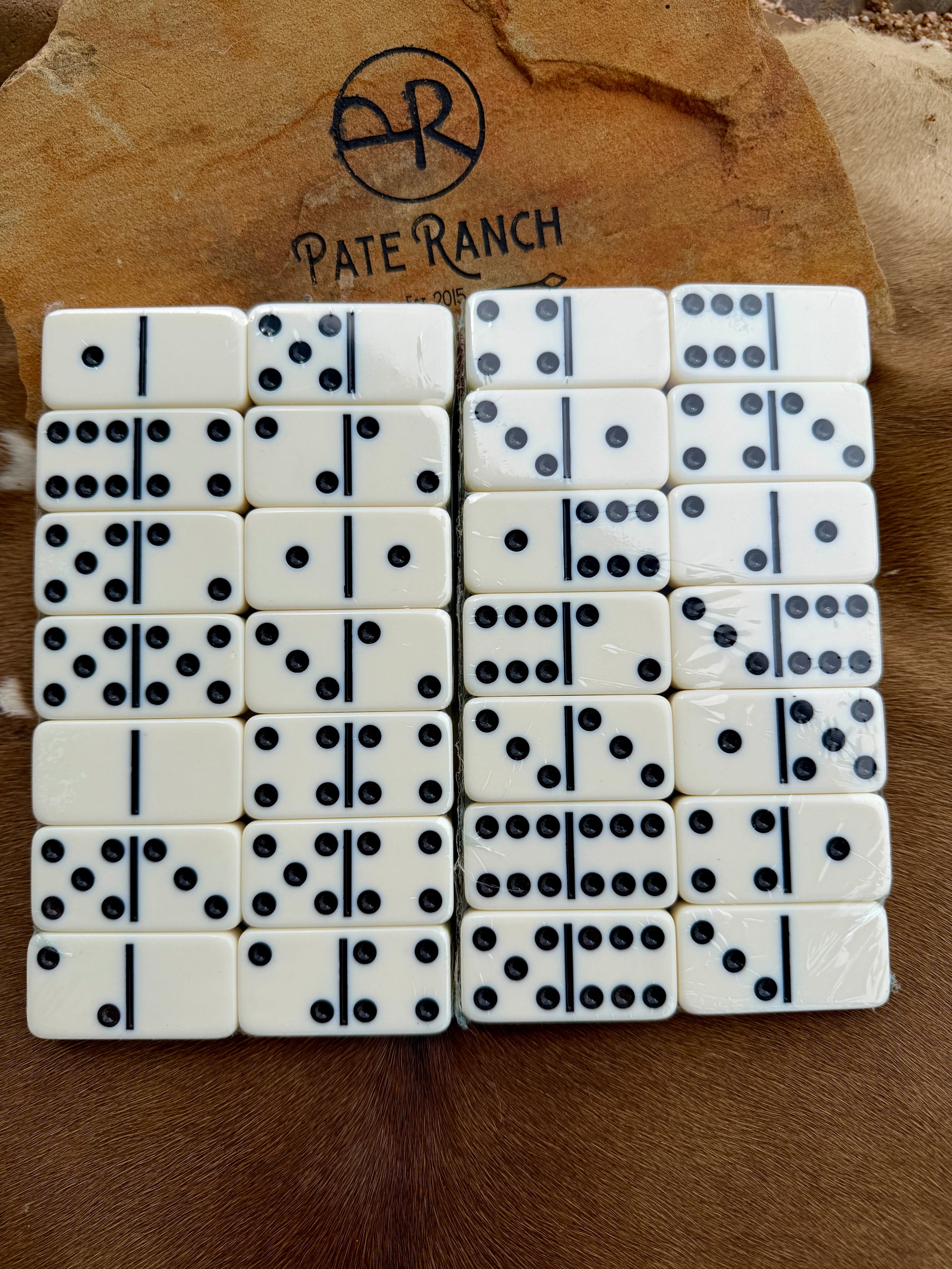 Set of dominoes with black dots on a wooden surface with 'Pate Ranch' branding.